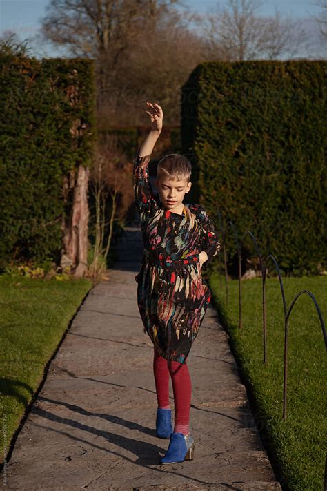 Boy Wearing Dress And Heels Dances Along A Garden Path By Stocksy