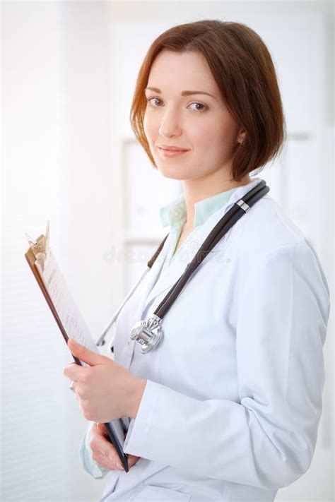 Young Brunette Female Doctor Standing With Clipboard And Smiling In