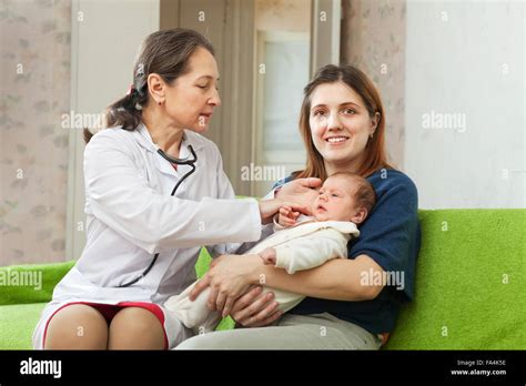 Mature Pediatrician Doctor Examining Newborn Baby On Mothers Arms In