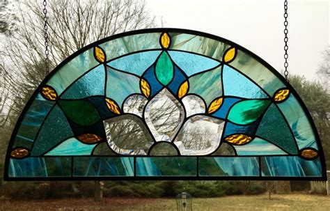 a stained glass window hanging from chains in front of some trees and grass on a cloudy day