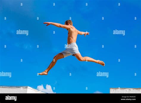 Young Man Doing Parkour Jump On The Blue Sky Background On Sunny Summer