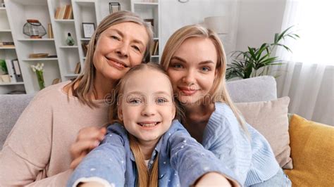 Happy Grandmother Mother And Granddaughter Are Sitting On The Sofa In The Living Room Taking