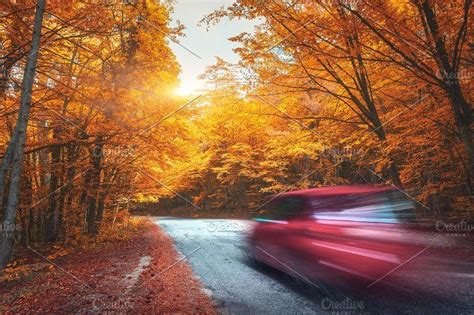 Blurred Car Going Mountain Road In Autumn Forest At Sunset By Den