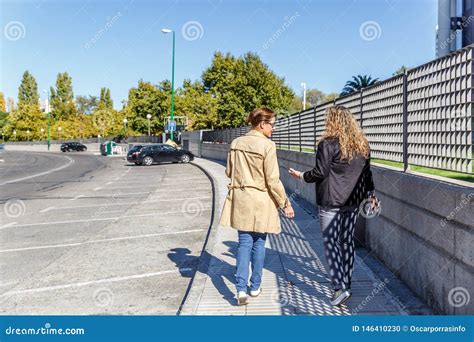 Two Female Friends Chat While Walking Quietly Down A Street On A