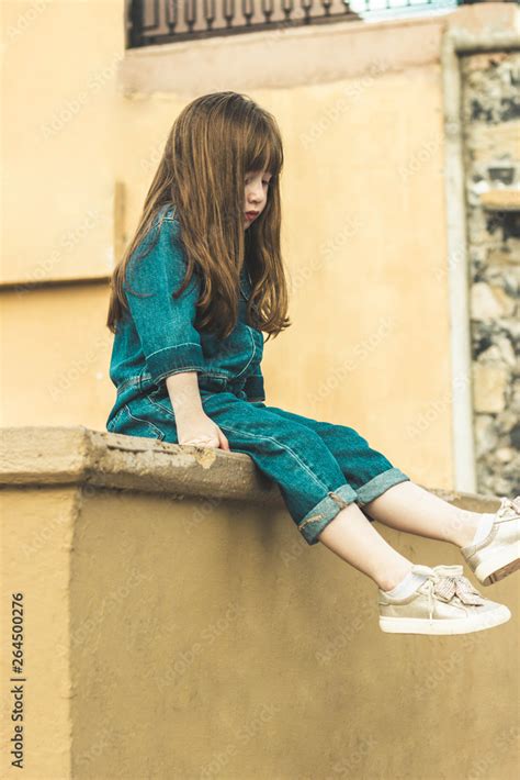 Shy Little Girl Sitting Down Looking At Her Feet In Denim Clothes