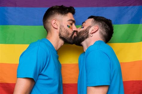 pareja de homosexuales de hombres besándose en una bandera de arcoiris lgbt foto gratis