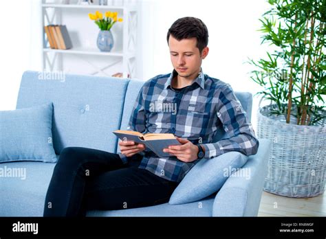 Handsome Young Man Guy Reading A Book Sitting On The Couch In His