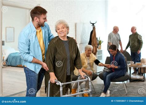 Care Worker Helping To Woman With Walker In Geriatric Hospice Stock