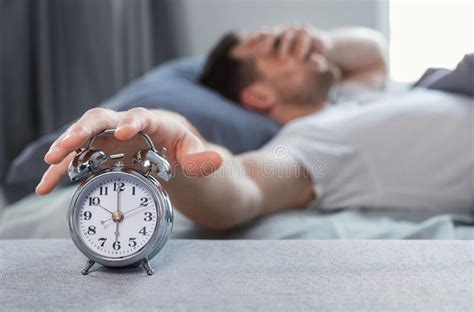 Sleepy Man Turning Off Alarm Clock Waking Up In Bed Indoors Stock Image