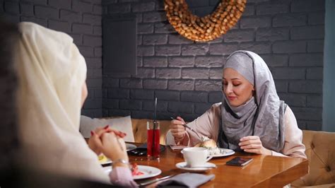 A Young Muslim Women Sitting Eating And Talking In Modern Cafe Stock