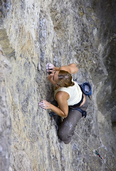 Female Rock Climber Clinging To A Cliff As She Battles Her Way Up Stock