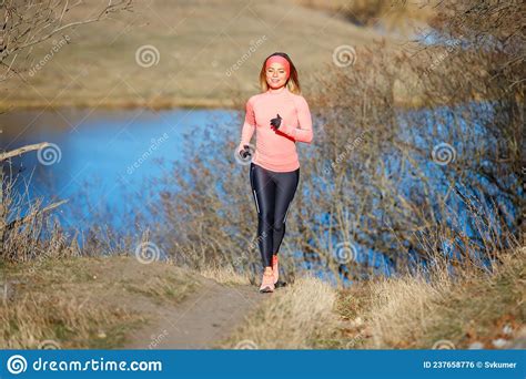 Young Woman Jogging In The Park Near The Pond In The Cold Sunny Morning