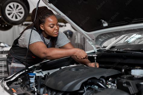 Black Female Mechanic Working Under The Hood At Repair Garage Portrait