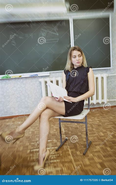 Strict Young Blonde Teacher Sits On A Chair Crossing Her Legs Stock