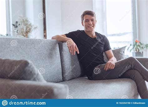 Brooding Young Man Sitting On The Couch In His Living Room Stock Photo