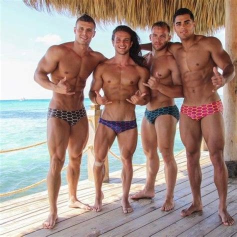 Three Men In Swimsuits Posing For The Camera On A Pier By The Ocean