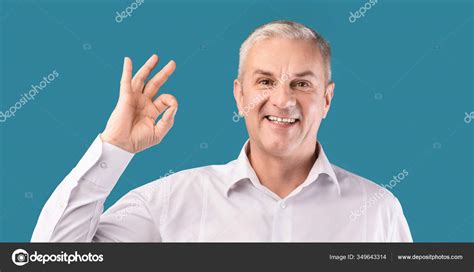 Smiling Elderly Man Gesturing Ok Sign At Blue Studio Stock Photo By