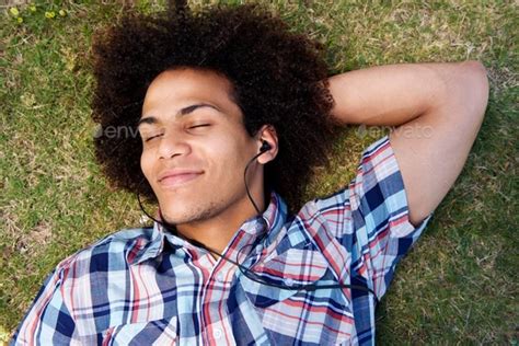 Young Man Lying Down On Grass Listening To Music Stock Photo By