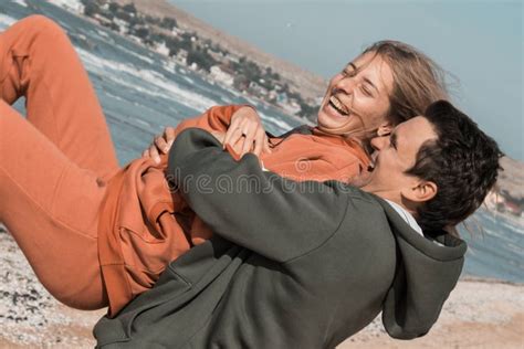 The Guy And The Girl Hug And Look At Each Other With Love On The Beach Against The Backdrop Of