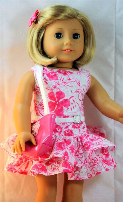 a doll with blonde hair wearing a pink dress and carrying a pink handbag in her left hand
