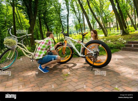 Young Man In Green And Red Plaid Shirt And His Girlfriend Trying To Fix A Bike After Biking In A