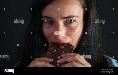 portrait of a sexy brunette woman with red lips who eroticly and playfully eats black chocolate