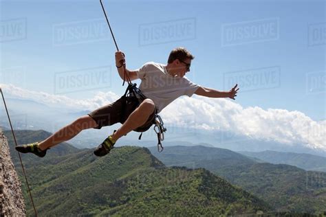 Young Man Hanging From A Cliff In The Mountains Stock Photo Dissolve