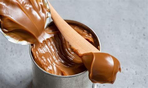 A Spoon Full Of Peanut Butter In A Metal Can With Some Caramel On Top