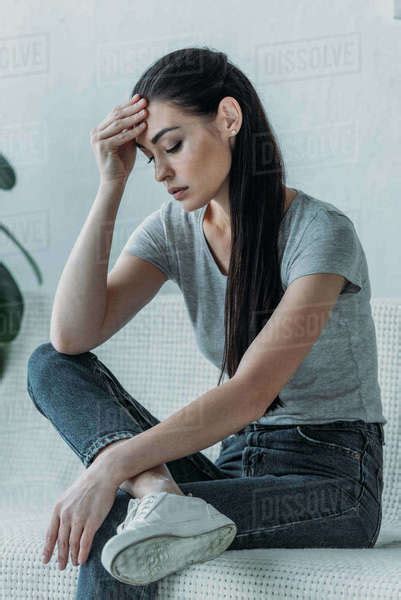 Upset Young Woman With Hand On Forehead Sitting On Couch And Looking