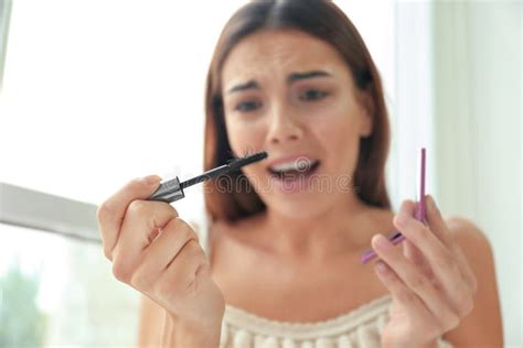 Emotional Young Woman Holding Mascara Brush With Eyelashes Indoors