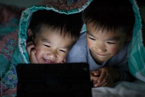 Asian Kids Watching On Tablet Computer In Bed At Home By Stocksy