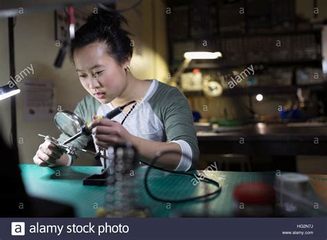 Female Electronics Engineer Using Soldering Iron At Workbench In Stock