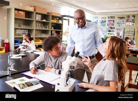 Los Estudiantes De Secundaria Con El Tutor Utilizando Microscopio En