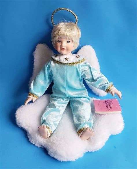 An Angel Doll Sitting On Top Of A Fluffy White Cloud With A Book In It