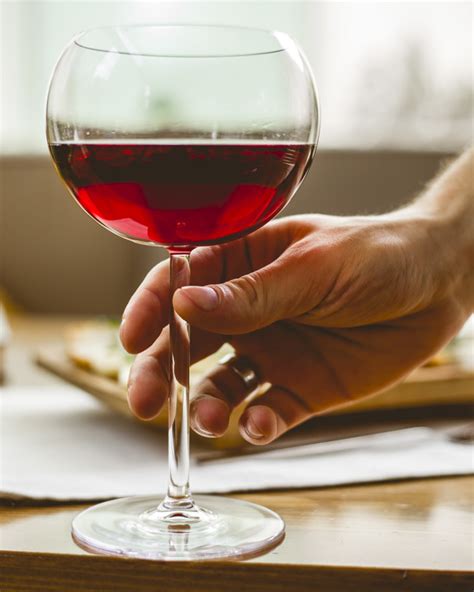 Do you hold wine glasses at the stem or bowl? Man are holding the glass with red wine side view | Free Photo