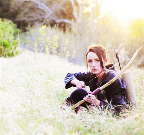 A Woman Sitting In The Grass With A Bow And Arrow