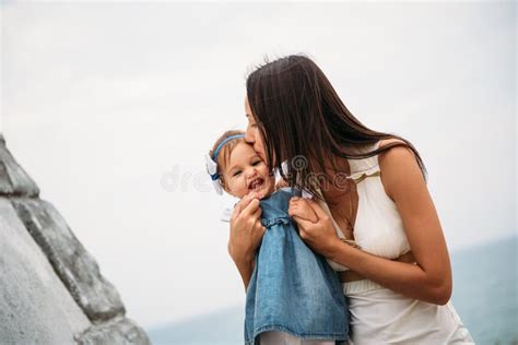 Happy Young Mother With A Small Daughter In Hands Hugging Near To The Lighthouse Outdoors