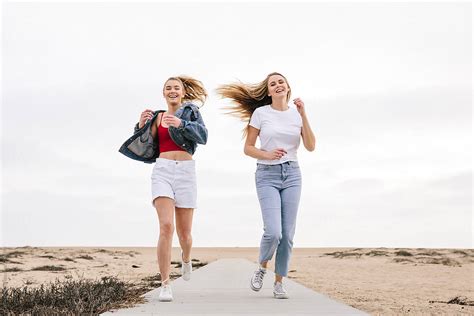 Two Sisters Running On A Sidewalk Laughing And Smiling At The Beach