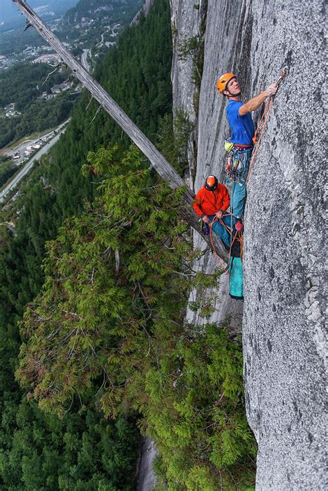 Two Men Rock Climbing While Belaying From Hanging Tree On Exposed Wall
