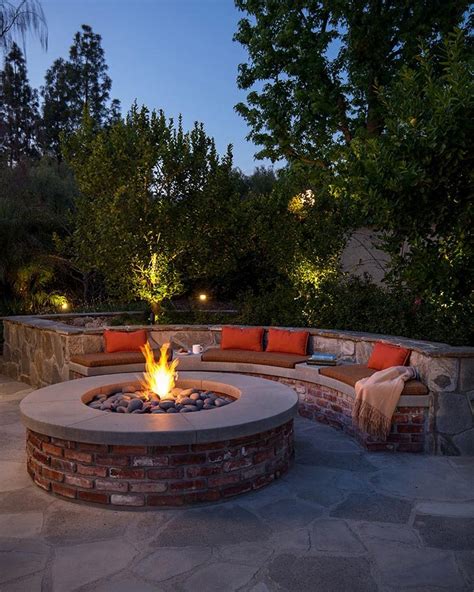 An Outdoor Fire Pit Surrounded By Brick Walls And Seating Around It At Night With Trees In The