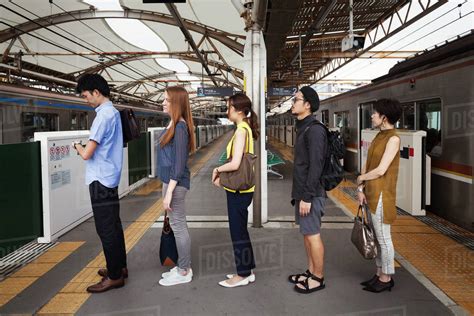 Five People Standing In A Row On A Subway Platform Waiting In Line