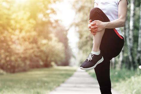 Young Fitness Woman Runner Stretching Legs Before Run On Grass Stock