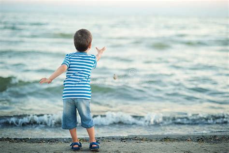 The Little Boy By The Sea Throws Stones In Water Sunset Stock Image