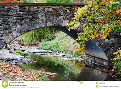 A Stone Bridge With A Creek Running Under With Beautiful Reflections In