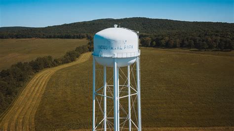 Water Tower In Green Field Behind Mountain · Free Stock Photo