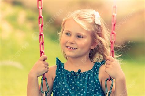 portrait of a cute little blond girl riding on a swing on a playground outdoors photo background