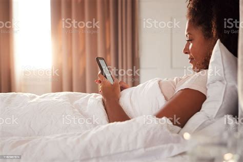 Woman Sitting Up In Bed Looking At Mobile Phone After Having Woken Up