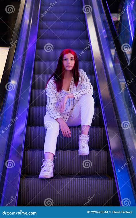 linda adolescente avermelhada sentada em degraus da escada rolante na rua da cidade iluminada