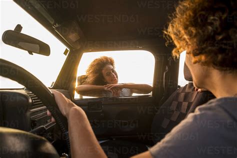 Young Woman Leaning On Car Window Looking Inside To Driver Stock Photo