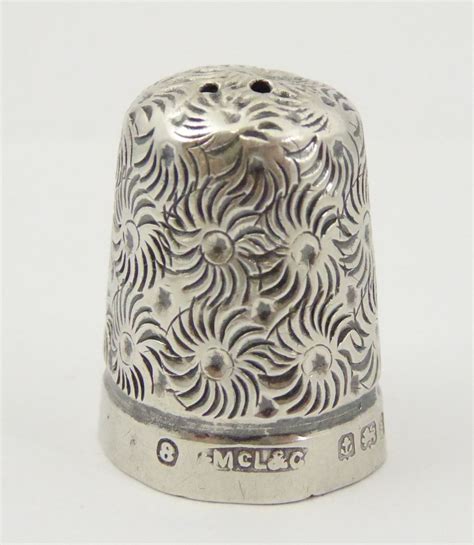 An Antique Silver Thimble With Floral Designs On The Front And Sides